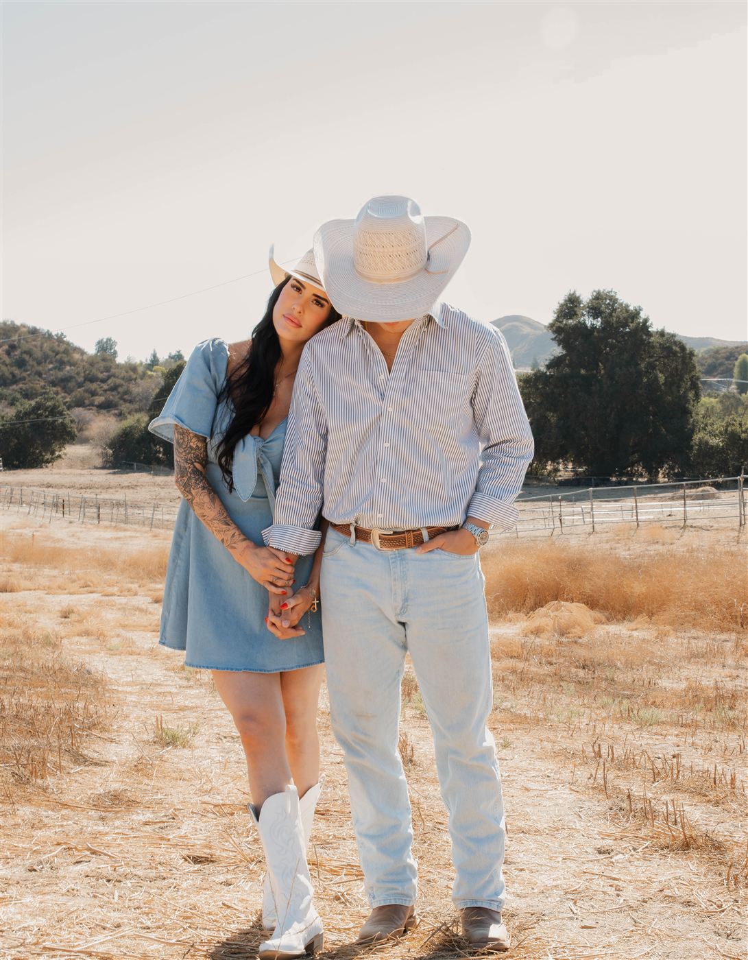 Couple in cowboy hats and denim leaning into each other in a golden ranch field