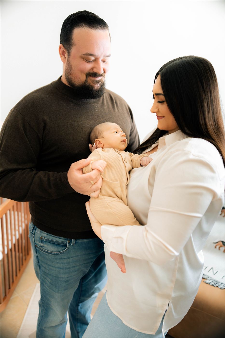 The Perkins parents smiling down at their newborn son, held between them in a tan knit romper