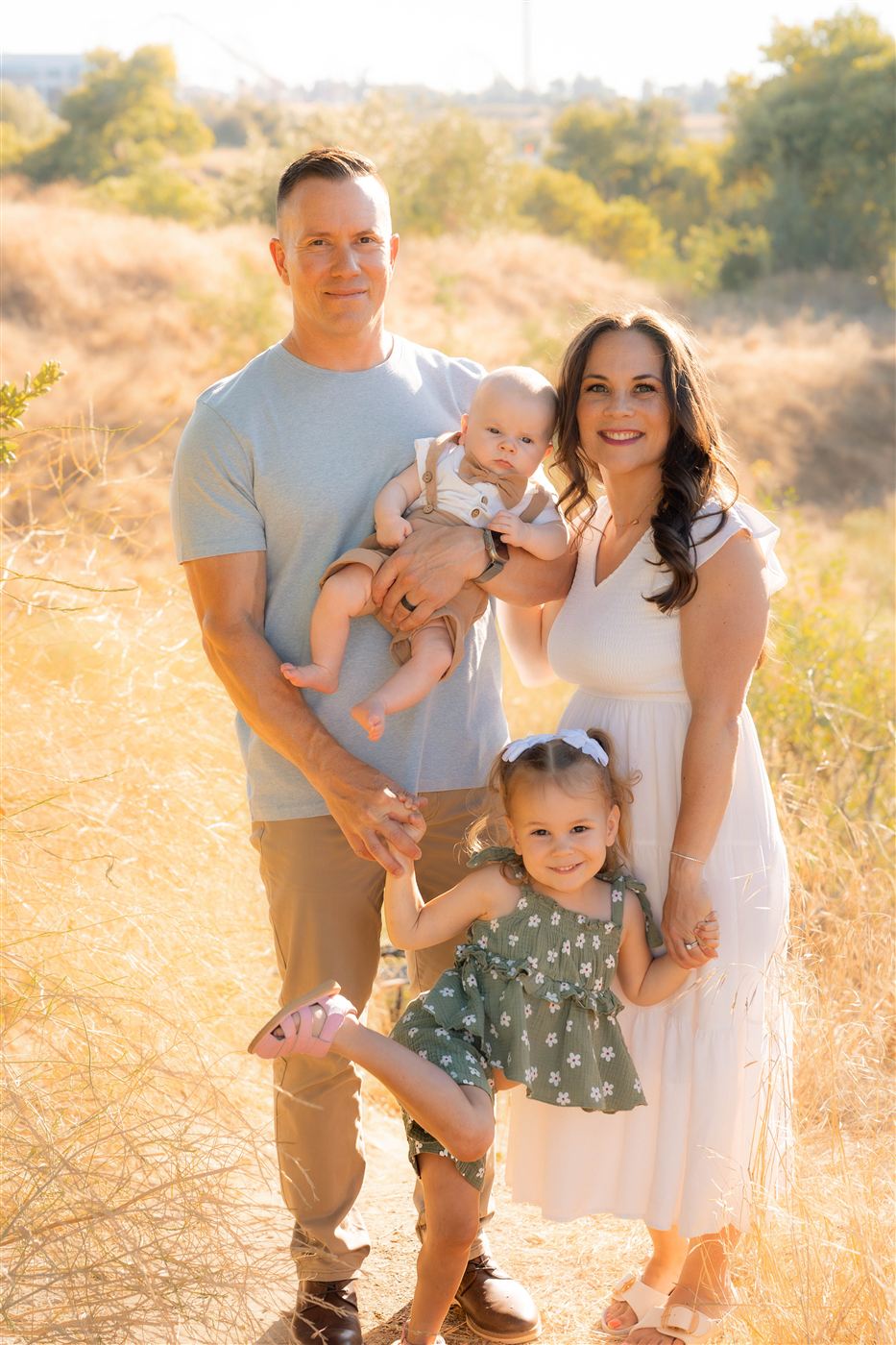 The Salinas family, parents holding their baby son and toddler daughter in a golden grassy field