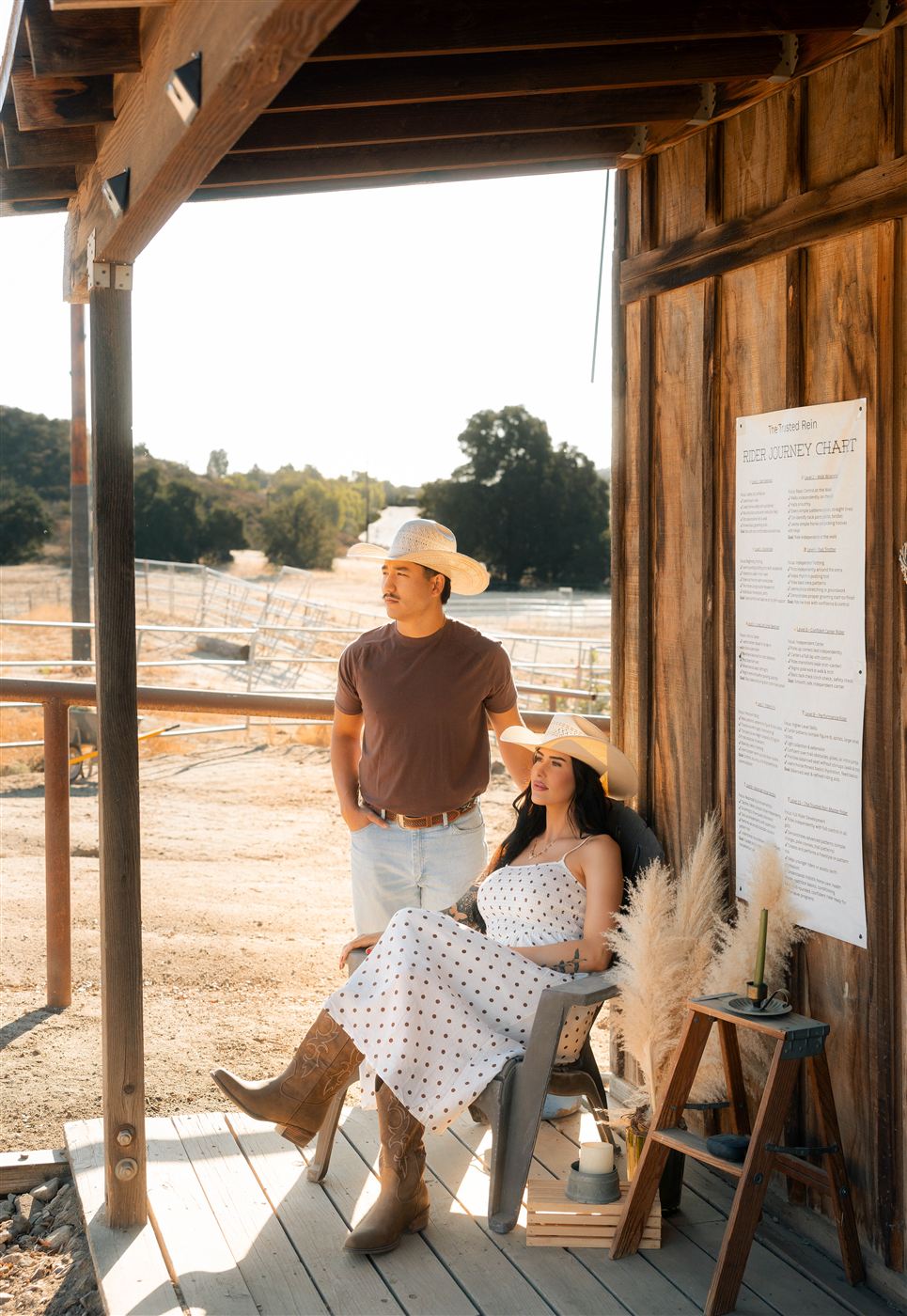 Breanna and Mason, an expecting couple in cowboy hats, on a rustic ranch porch beside a rider journey chart